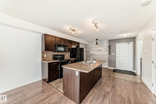 The kitchen features dark wood cabinetry, black appliances, and a central island with a granite-style countertop and an integrated sink - 301 103 Ambleside Drive, Edmonton, AB - Indoor Photo Showing Kitchen