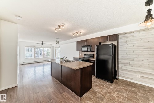 Open concept living area featuring dark wood flooring, a kitchen island with a double sink and light-colored countertop, and dark wood kitchen cabinetry - 301 103 Ambleside Drive, Edmonton, AB - Indoor Photo Showing Kitchen With Double Sink
