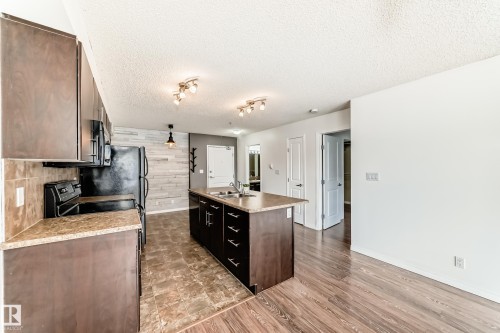 The kitchen features dark wood cabinetry, a central island with a sink, and a black refrigerator and stove - 301 103 Ambleside Drive, Edmonton, AB - Indoor Photo Showing Kitchen With Double Sink