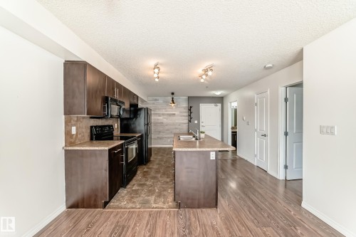 The property features a kitchen with dark wood cabinetry, black appliances, and a central island with a sink - 301 103 Ambleside Drive, Edmonton, AB - Indoor Photo Showing Kitchen With Double Sink