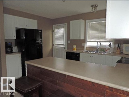 The kitchen features white cabinetry, a black refrigerator, and a double basin sink - 1318 8 Avenue, Cold Lake, AB - Indoor Photo Showing Kitchen With Double Sink