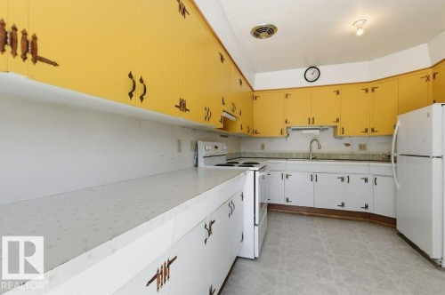 The kitchen features yellow upper cabinetry and white lower cabinetry, providing ample storage - 10459 66 Avenue, Edmonton, AB - Indoor Photo Showing Kitchen
