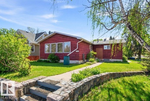 The property features a stone retaining wall and steps leading to a pathway, a vibrant green lawn, and mature trees - 10459 66 Avenue, Edmonton, AB - Outdoor