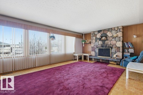 The living area features a stone fireplace with a hearth, wood paneling, and large windows with vertical blinds - 10459 66 Avenue, Edmonton, AB - Indoor Photo Showing Other Room With Fireplace