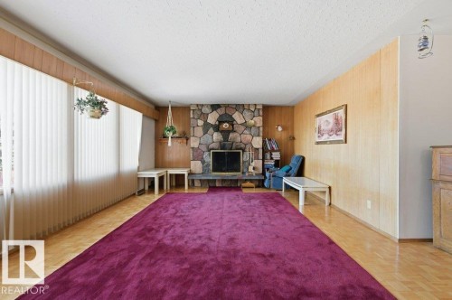The living room features wood paneling, a stone fireplace, and light-colored flooring - 10459 66 Avenue, Edmonton, AB - Indoor Photo Showing Living Room With Fireplace