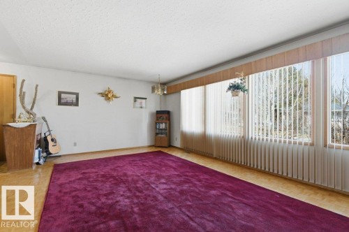 The spacious living area features large windows with vertical blinds, providing natural light, and a vibrant magenta area rug over parquet flooring - 10459 66 Avenue, Edmonton, AB - Indoor Photo Showing Other Room