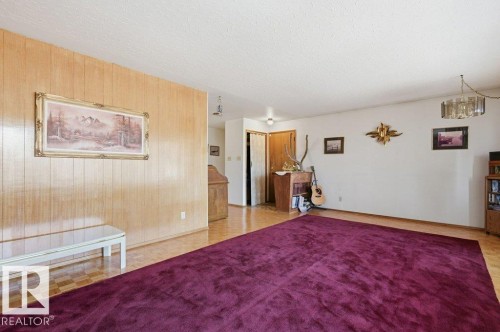 The expansive living area features parquet flooring, a wood-paneled accent wall, and a ceiling light fixture - 10459 66 Avenue, Edmonton, AB - Indoor