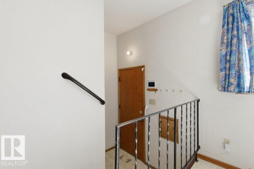 The property features a staircase with a wrought iron railing, a wooden door, and a wall-mounted handrail - 10459 66 Avenue, Edmonton, AB - Indoor Photo Showing Other Room