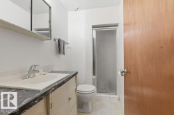 Bathroom featuring a vanity with an integrated sink and a dark countertop, a toilet, and a stand-up shower with a frosted glass door - 