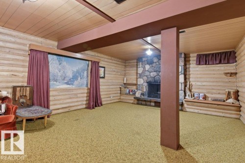 Rustic style interior featuring wood paneled walls and ceiling, green carpet flooring, a stone fireplace, and exposed support beams - 10459 66 Avenue, Edmonton, AB - Indoor Photo Showing Other Room