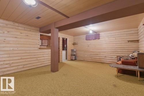 This spacious room features log-style paneling on the walls, a paneled ceiling, and carpeting - 10459 66 Avenue, Edmonton, AB - Indoor