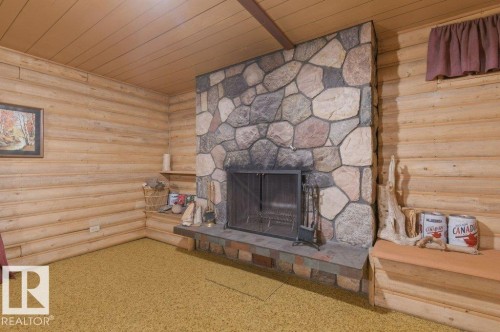 Living area featuring a stone fireplace with a metal screen, wood paneled walls, and a wood ceiling - 10459 66 Avenue, Edmonton, AB - Indoor With Fireplace