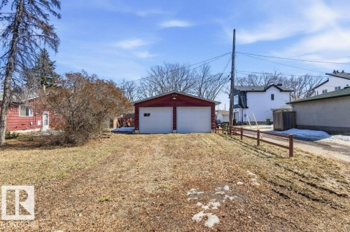 The property includes a detached red garage with two white doors and a window, situated on a lot with a dirt and grass surface - 10459 66 Avenue, Edmonton, AB - Outdoor