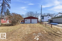The property includes a detached red garage with two white doors and a window, situated on a lot with a dirt and grass surface - 