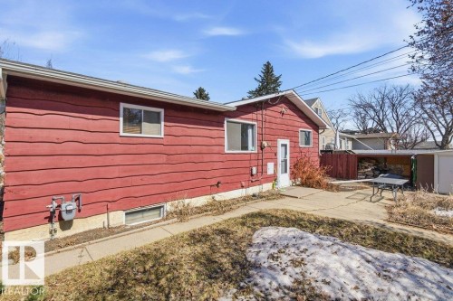 The property features red horizontal siding and a white side door, with a paved area leading to an uncovered patio - 10459 66 Avenue, Edmonton, AB - Outdoor With Exterior