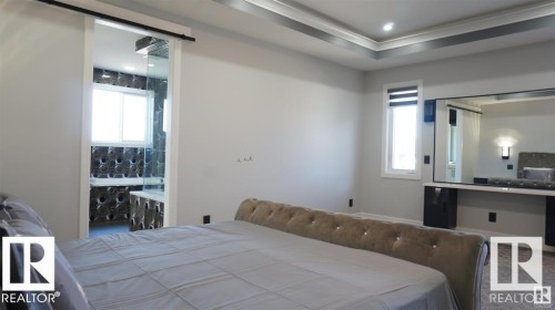 The bedroom features a sophisticated tray ceiling, a large window, and a dressing table with an integrated mirror - 707 180 Street, Edmonton, AB - Indoor Photo Showing Bedroom