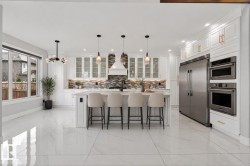 Gourmet kitchen featuring a substantial central island with seating, white shaker cabinetry, stainless steel appliances, and large format polished tile flooring - 