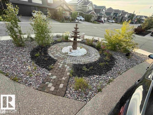 The property features a landscaped rock garden with a tiered water fountain, surrounded by a circular paved path and decorative white stones - 707 180 Street, Edmonton, AB - Outdoor