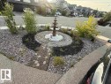 The property features a landscaped rock garden with a tiered water fountain, surrounded by a circular paved path and decorative white stones - 707 180 Street, Edmonton, AB  - Outdoor 