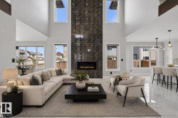 Open-concept living area with a double-height ceiling and a gas fireplace set into a floor-to-ceiling stone-look accent wall - 