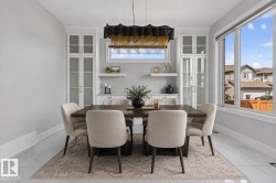 Dining area featuring a dark wood-finish dining table and upholstered chairs, recessed built-in cabinetry with glass panel doors, a large multi-pane window, and high-gloss tile flooring - 