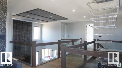 The property features an open landing with wood and glass railings, a decorative ceiling with recessed lighting, and a contemporary chandelier - 707 180 Street, Edmonton, AB - Indoor Photo Showing Other Room