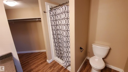 Bathroom featuring wood-look flooring, a shower with a patterned curtain, and an open closet space with shelving and a hanging rod - 2103 1601 8 Avenue, Cold Lake, AB - Indoor Photo Showing Bathroom