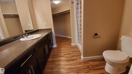 The property features a bathroom with a vanity, sink, and toilet, complemented by wood-look flooring and light-colored walls - 2103 1601 8 Avenue, Cold Lake, AB - Indoor Photo Showing Bathroom