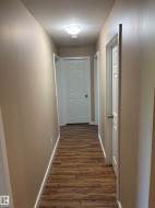 Hallway featuring wood-finish flooring, light tan walls, white trim, and multiple white panel doors - 