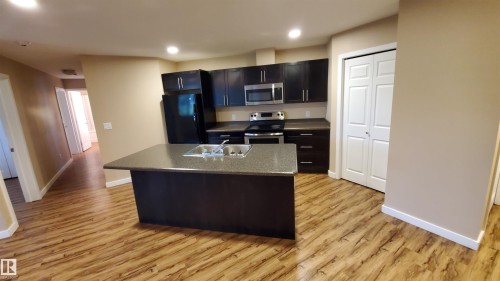 The kitchen features dark wood cabinetry, a central island with a sink, and stainless steel appliances - 2103 1601 8 Avenue, Cold Lake, AB - Indoor Photo Showing Kitchen