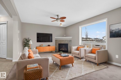 Living area featuring a fireplace with a stone surround, a large window providing views of the neighborhood, and a ceiling fan - 96 Dalquist Bay, Leduc, AB - Indoor Photo Showing Living Room With Fireplace