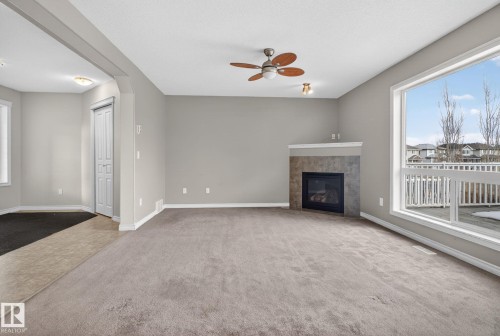 This inviting living space features light gray walls, a ceiling fan with wooden blades, and a corner fireplace with a stone surround - 96 Dalquist Bay, Leduc, AB - Indoor With Fireplace