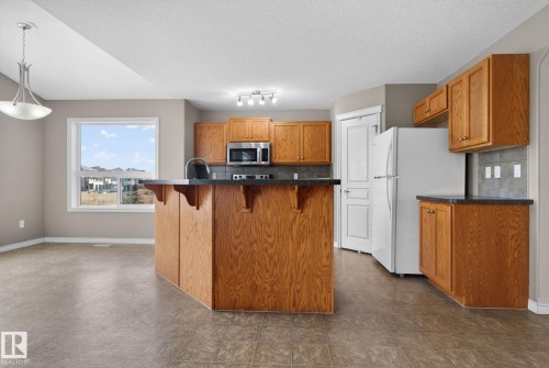 The kitchen features wooden cabinetry, dark countertops, and includes a stainless steel microwave and stove - 96 Dalquist Bay, Leduc, AB - Indoor Photo Showing Kitchen