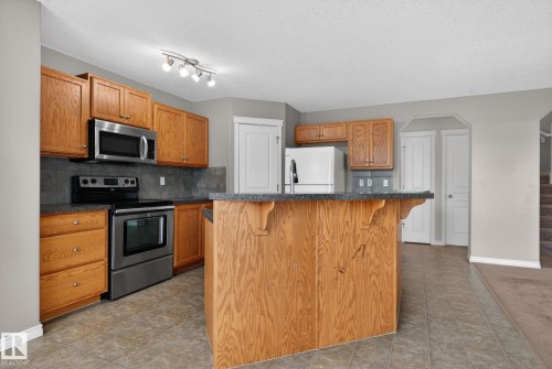 The kitchen features wood cabinetry, stainless steel appliances including an oven and microwave, and track lighting - 96 Dalquist Bay, Leduc, AB - Indoor Photo Showing Kitchen