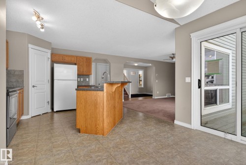 The kitchen features a functional island with a sink, wood cabinetry, and a refrigerator - 96 Dalquist Bay, Leduc, AB - Indoor Photo Showing Kitchen