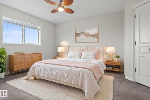 This bedroom features a ceiling fan with integrated lighting, a large window providing natural light, and soft grey carpeting - 96 Dalquist Bay, Leduc, AB - Indoor Photo Showing Bedroom