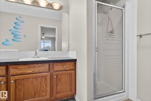 The bathroom features a vanity with a dark countertop and wooden cabinetry, a white ceramic sink with a chrome faucet, and a shower with a glass door - 96 Dalquist Bay, Leduc, AB - Indoor Photo Showing Bathroom