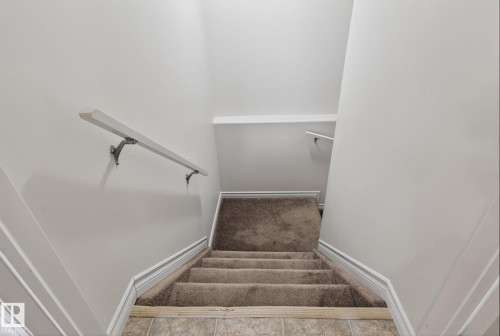 Stairwell featuring light gray walls, white handrails, and carpeted stairs leading down to tiled flooring - 96 Dalquist Bay, Leduc, AB - Indoor
