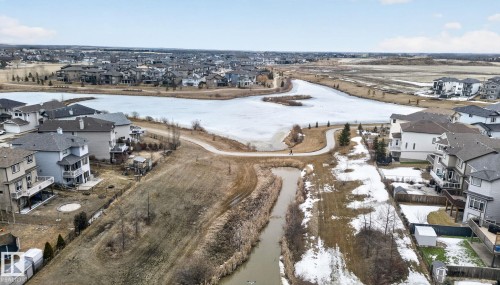 This aerial view showcases the property situated within a community featuring a frozen body of water and a paved pathway - 96 Dalquist Bay, Leduc, AB - Outdoor With View