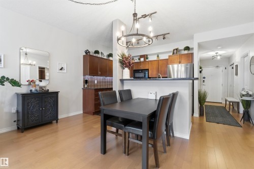 The property features light-colored flooring throughout, a kitchen with stainless steel appliances and dark wood cabinetry, and a dining area with a dark-colored table - 316 141 Festival Way, Sherwood Park, AB - Indoor Photo Showing Dining Room