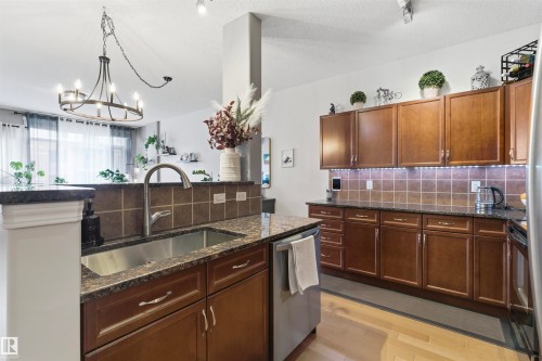 The kitchen features dark wood cabinetry, granite countertops, and a stainless steel sink with a gooseneck faucet - 316 141 Festival Way, Sherwood Park, AB - Indoor Photo Showing Kitchen