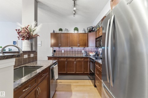 The kitchen features granite countertops, dark wood cabinetry, and stainless steel appliances, including a refrigerator and dishwasher - 316 141 Festival Way, Sherwood Park, AB - Indoor Photo Showing Kitchen With Double Sink With Upgraded Kitchen