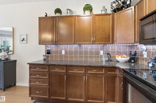 Kitchen featuring wood cabinetry, granite countertops, and a tiled backsplash with under-cabinet lighting - 316 141 Festival Way, Sherwood Park, AB - Indoor Photo Showing Kitchen