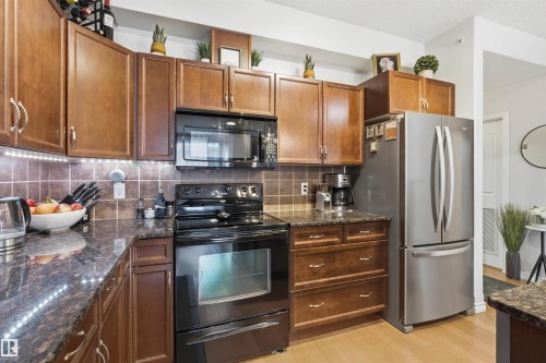 The kitchen features wood cabinetry, black appliances including an oven and microwave, a stainless steel refrigerator, and granite countertops - 316 141 Festival Way, Sherwood Park, AB - Indoor Photo Showing Kitchen
