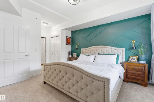 This space features a decorative accent wall with a geometric pattern, neutral carpeting, and white doors - 316 141 Festival Way, Sherwood Park, AB - Indoor Photo Showing Bedroom