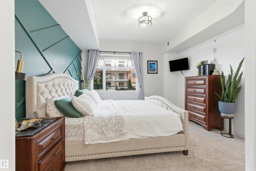 This bedroom features a decorative accent wall with geometric paneling, a large window with drapes, and plush carpeting - 316 141 Festival Way, Sherwood Park, AB - Indoor Photo Showing Bedroom