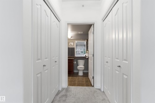Hallway featuring light gray carpet, white bi-fold doors, and a partial view of a bathroom with brown tile floors and a white toilet - 316 141 Festival Way, Sherwood Park, AB - Indoor Photo Showing Other Room