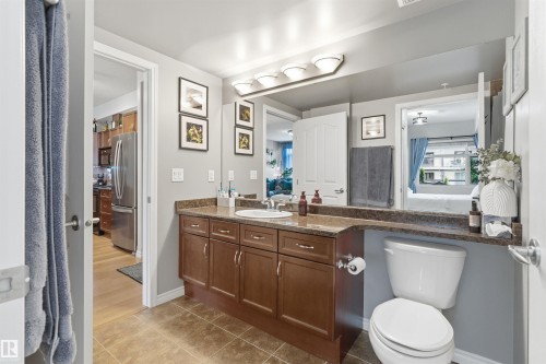 Bathroom featuring a vanity with a white basin and wood cabinetry, a large mirror, and tiled flooring - 316 141 Festival Way, Sherwood Park, AB - Indoor Photo Showing Bathroom