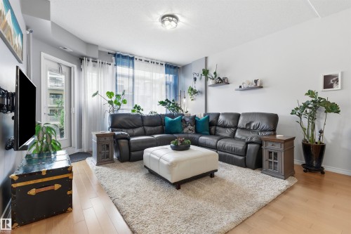 Living room featuring light wood flooring, a textured area rug, and a large window with sheer and blue curtains - 316 141 Festival Way, Sherwood Park, AB - Indoor Photo Showing Living Room