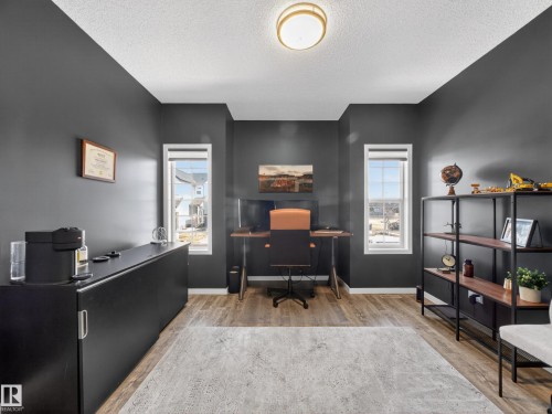 This versatile room features warm-toned flooring, dark-painted walls, and two windows providing natural light - 3210 Chernowski Way, Edmonton, AB - Indoor Photo Showing Office